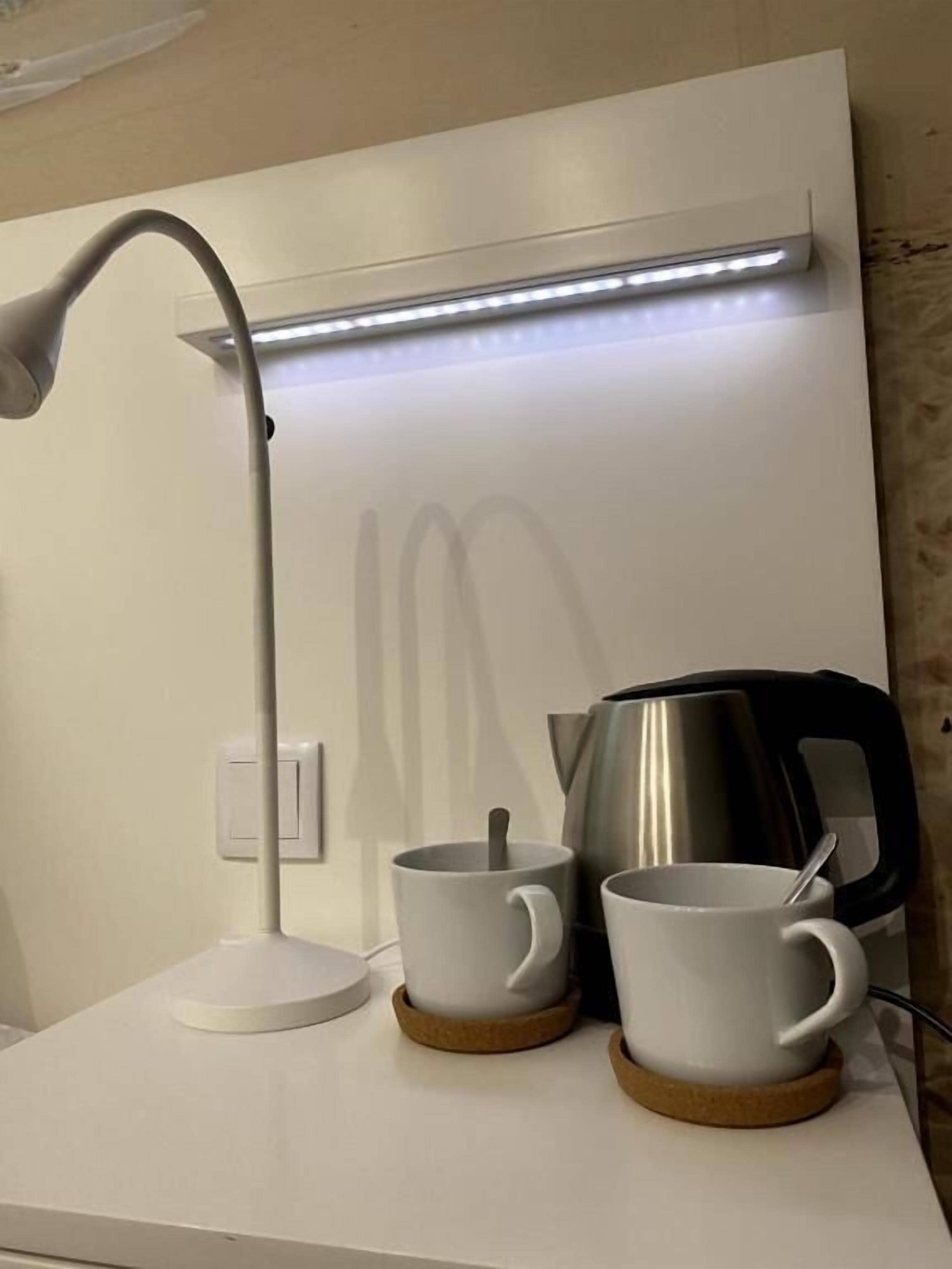 Een moderne werkruimte met een bureaulamp, twee witte mokken en een roestvrijstalen waterkoker op een witte tafel.