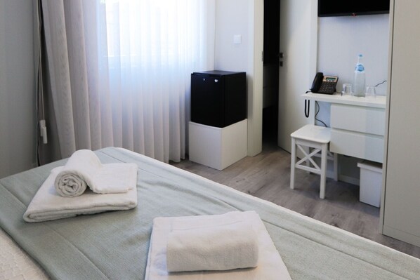A hotel room with a bed, a desk, a chair, a television, and a minibar.