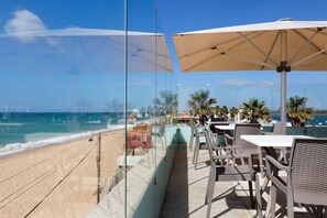 Une terrasse au bord de la plage, dotée de sièges et de parasols, avec vue sur l’océan.