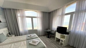 Quarto de hotel com duas camas, uma mesa, televisão e janelas amplas com cortinas.