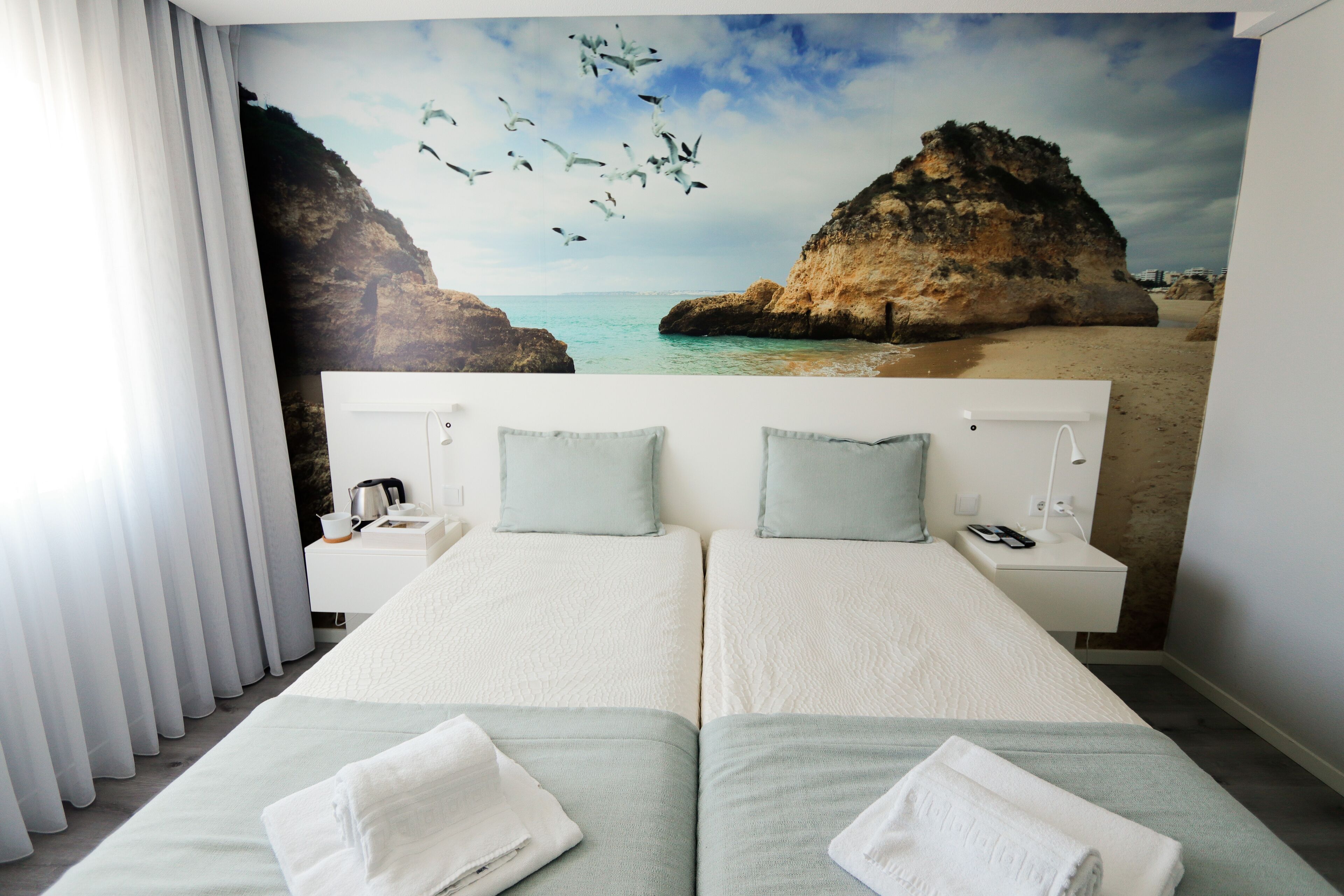 Habitación doble con dos camas, una mesita de noche con lámpara y un mural de playa.