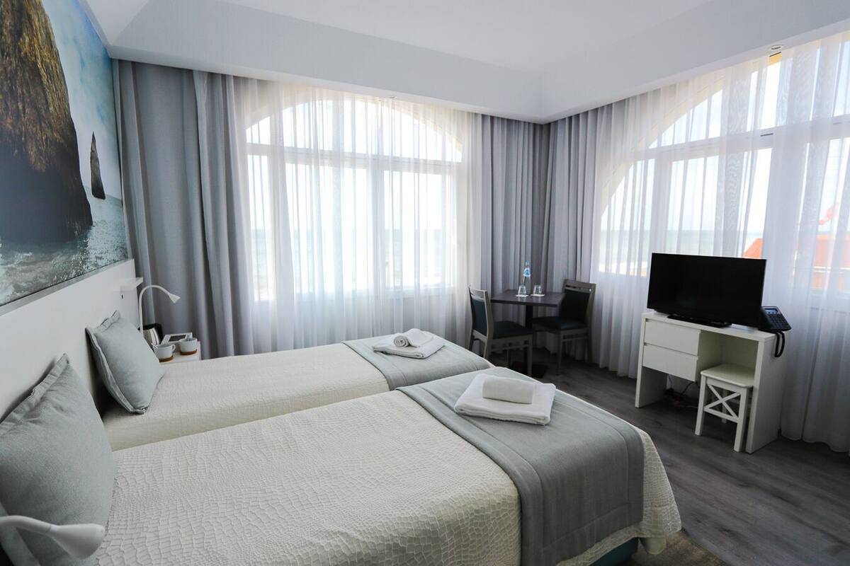 A hotel room with two beds, a desk with a chair, a television, and a painting on the wall.