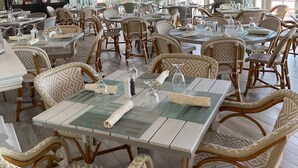 A spacious dining area with wicker chairs and tables, large windows, and a decorative ceiling.