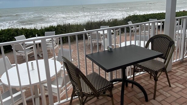 A covered patio with a table and chairs, overlooking the ocean.