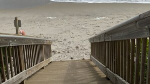 A wooden boardwalk leading to a sandy beach with waves crashing onto the shore.