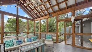 Un patio exterior techado con vigas de madera, amplios ventanales y una zona de estar rústica con cojines y una mesita de centro.