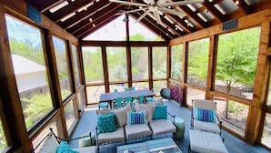 Una terraza techada al aire libre con vigas de madera, ventilador de techo y varias zonas de estar, incluyendo sofás y sillones.