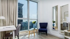 Et moderne hotelværelse med et stort vindue, et skrivebord med stol, en blå lænestol og et lille bord med en vase.
