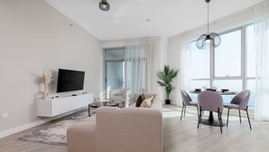 En moderne stue med sofa, fjernsyn, spiseplads og store vinduer.