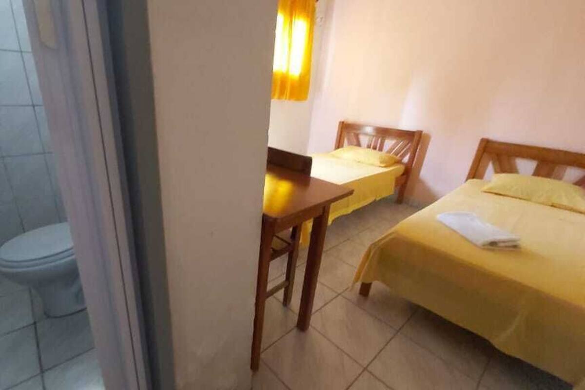 Una habitación pequeña con inodoro, una mesa y dos camas.