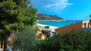 A coastal view with a beach, a mountain, and buildings in the foreground.