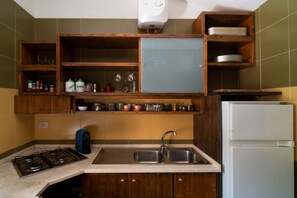 Een keuken met houten kastjes, een gasfornuis, een spoelbak en een witte koelkast.