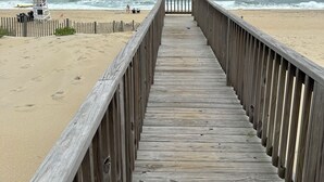 Una passerella in legno conduce a una spiaggia con una postazione di salvataggio e un cartello con la scritta 'LIFEGUARD HEAD'.