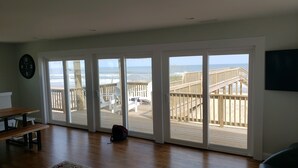 Una stanza con un'ampia porta scorrevole in vetro che dà su un terrazza in legno con vista sulla spiaggia e sull'oceano.