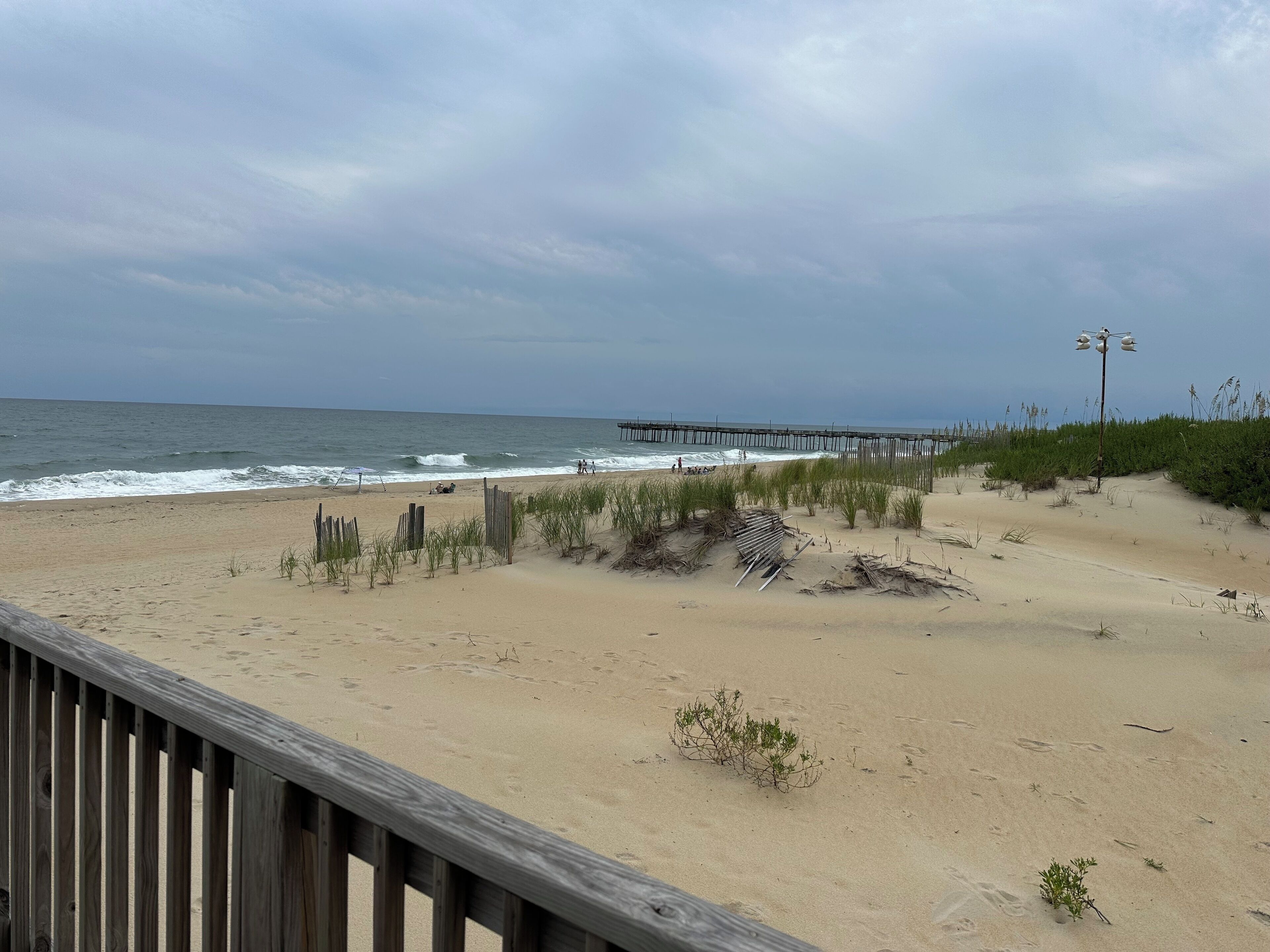 Ein Strand mit einer Holzpromenade, einem Steg und vereinzelter Vegetation.