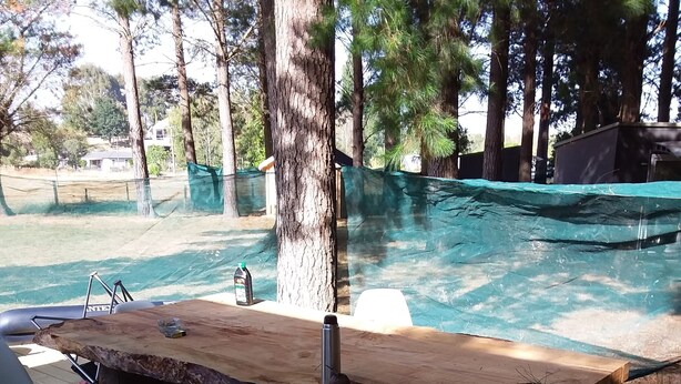 A wooden deck with a table and chairs, surrounded by trees and a swimming pool. - The pines 4  x private chalets (Cheviot)
