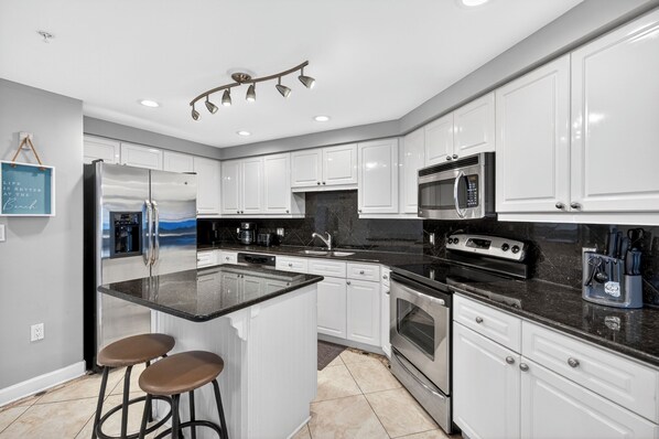 A modern kitchen with white cabinets, stainless steel appliances, a central island with stools, and a pendant light fixture.