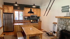 A kitchen with wooden cabinets, a stainless steel refrigerator, a stone fireplace, and a stone wall. - Cozy home in heart of Sunriver w/ hot tub, close to Mt Bachelor (Sunriver)