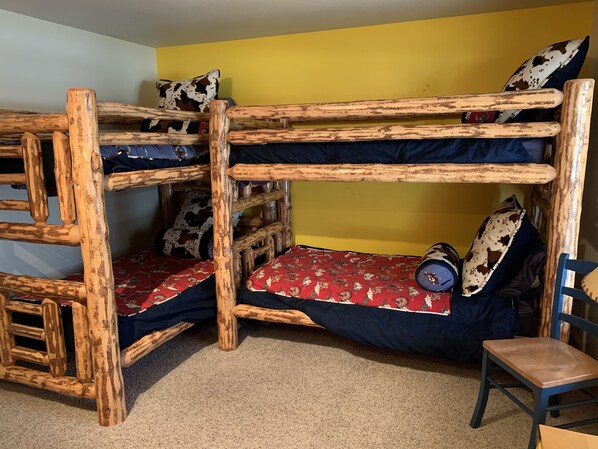 A bunk bed with a rustic wooden frame, a red patterned bedspread, and cowhide pillows.