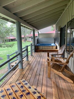 A covered porch with wooden flooring, a hot tub, and wooden chairs.
