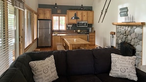 A modern kitchen with wooden cabinets, a stainless steel refrigerator, a microwave, and a stone fireplace. - Cozy home in heart of Sunriver w/ hot tub, close to Mt Bachelor (Sunriver)