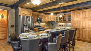 A kitchen with wooden cabinets, a large island with bar stools, stainless steel appliances, and pendant lighting. - Luxurious Expansive Cabin Escape on Gull Lake! (Nisswa)