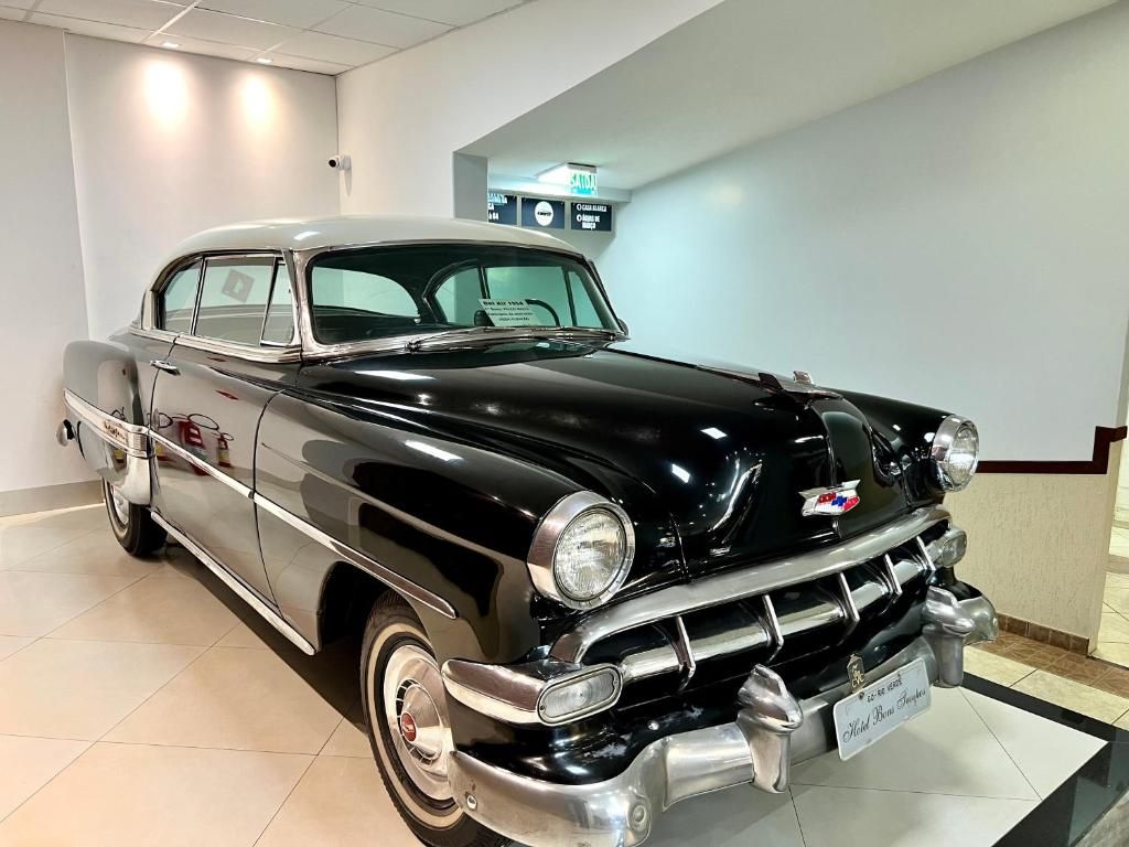 A classic black car in a showroom with a clean, white interior and a sign indicating a car sale.
