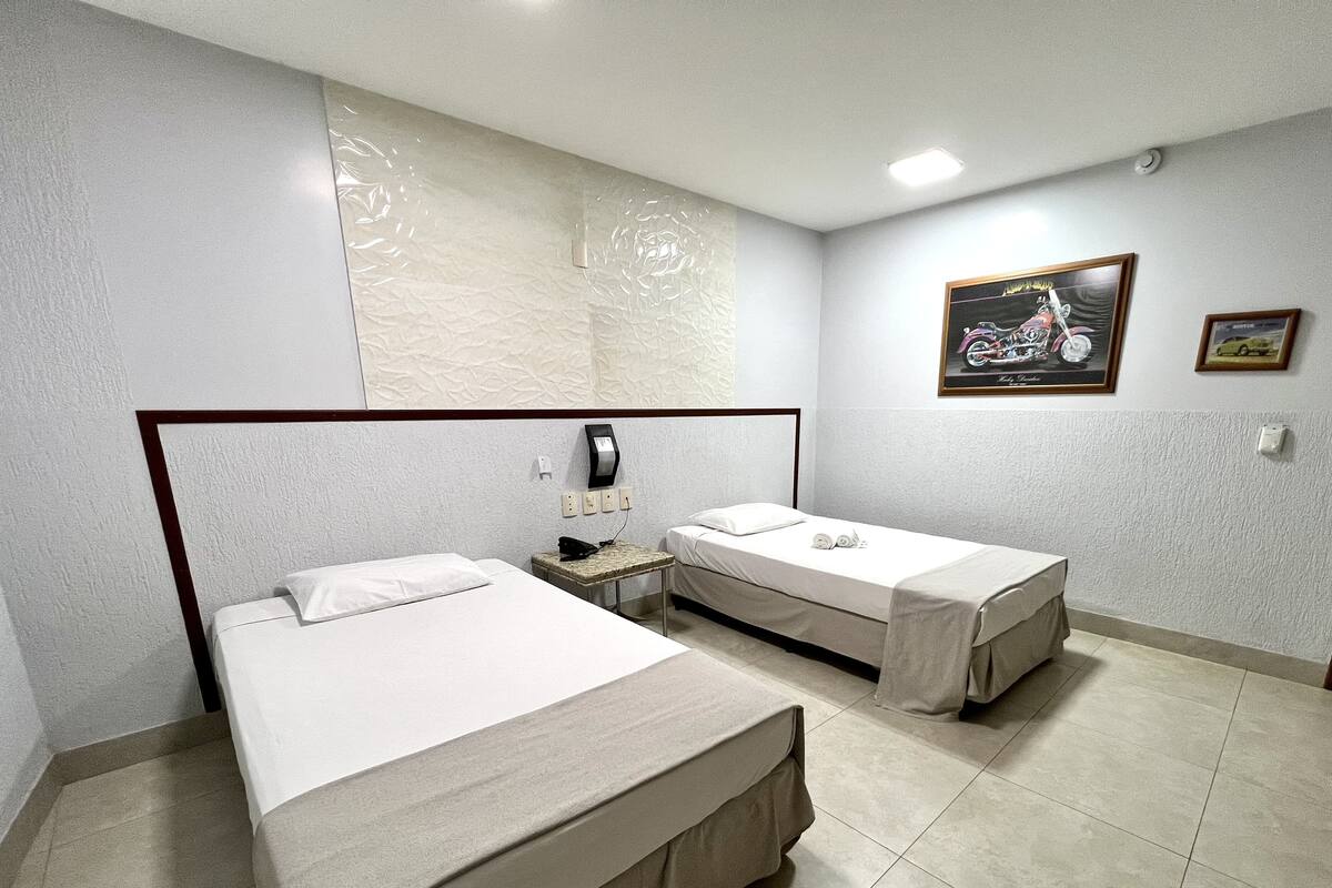 A hotel room with two beds, a small table, a phone, and a wall-mounted light.