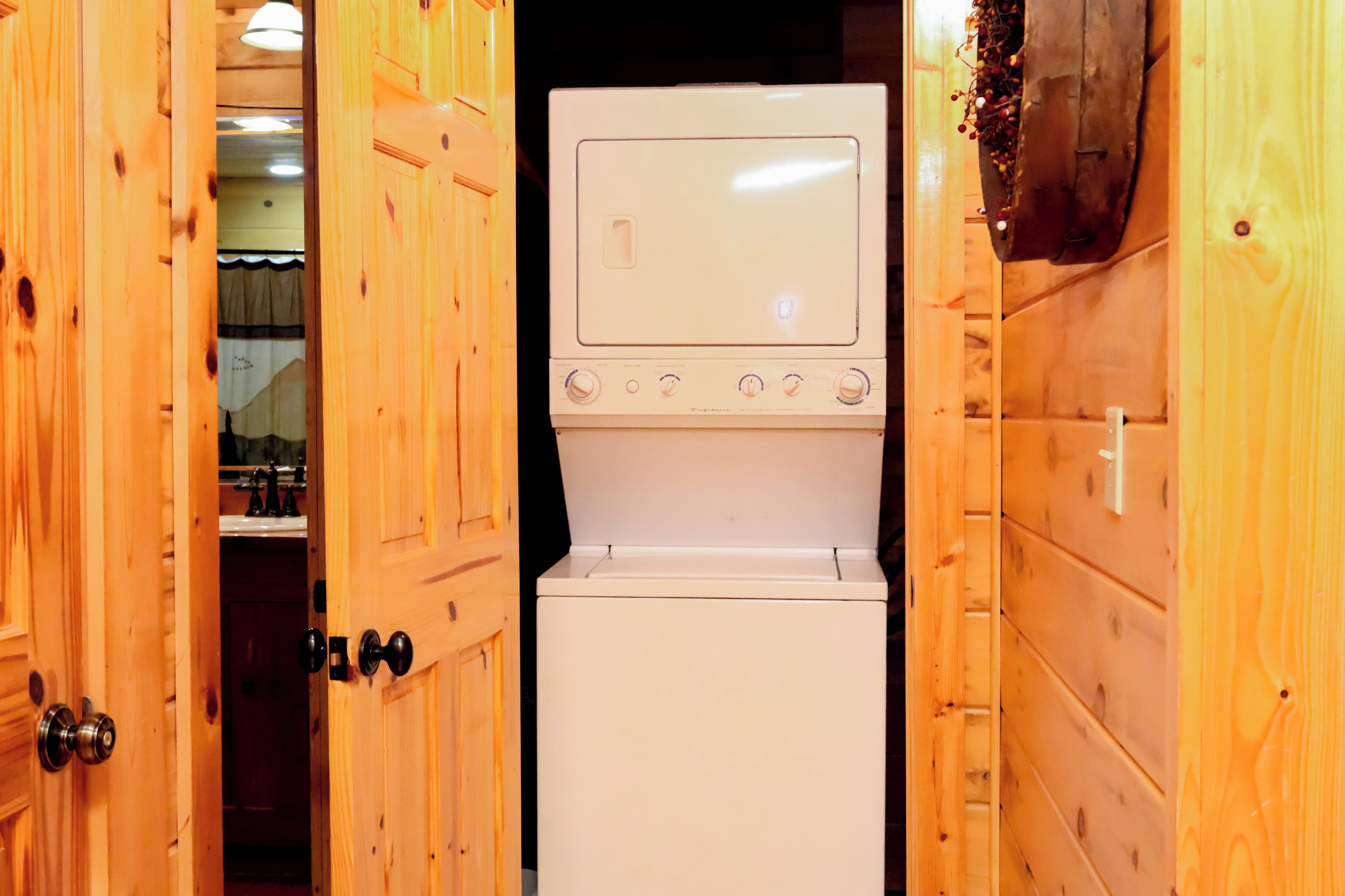 Lavatrice e asciugatrice bianca e compatta, integrate nel muro, in una stanza dal sapore rustico con porta che conduce al bagno.