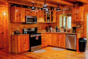 A wooden cabin interior with a kitchen featuring wooden cabinets, a microwave, stove, oven, and a dishwasher.