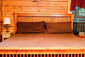 A wooden bed with a quilted mattress and two pillows, a bedside lamp, and a nightstand with a decorative item.