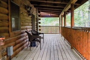 A wooden cabin with a porch, two wicker chairs, and a wooden railing.