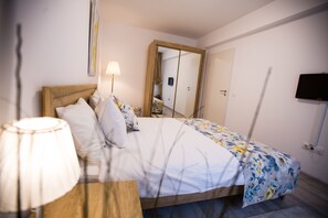 A neatly made bed with a floral bedspread, a bedside lamp, and a mirror above it. - Apartment Ella (Brasov)
