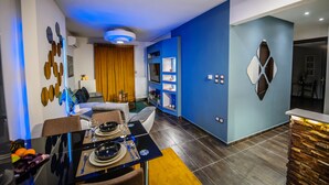 A modern living room with a dining area, featuring a blue accent wall, a built-in shelving unit, and a contemporary light fixture. - One of a kind LUXURY Apartment in City Center Near HELEXPO (Thessaloniki)