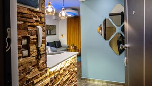 A modern reception area with a stone wall, a counter with a phone, and a seating area with a sofa and a table. - One of a kind LUXURY Apartment in City Center Near HELEXPO (Thessaloniki)