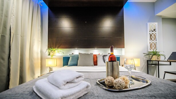 A neatly made bed with a tray of eggs and a bottle of wine, a lamp, and a plant on the side. - One of a kind LUXURY Apartment in City Center Near HELEXPO (Thessaloniki)