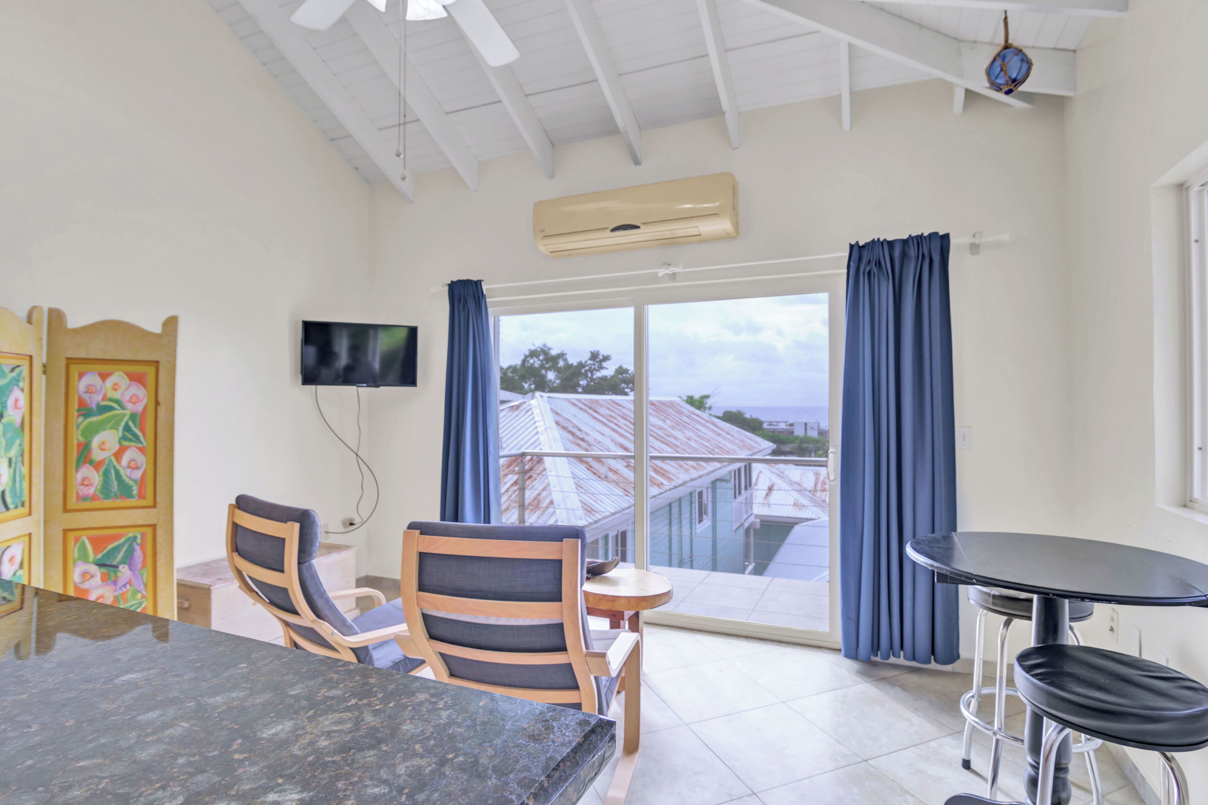 Una habitación con una mesa de comedor, dos sillas, un televisor y un balcón con vistas a la ciudad.