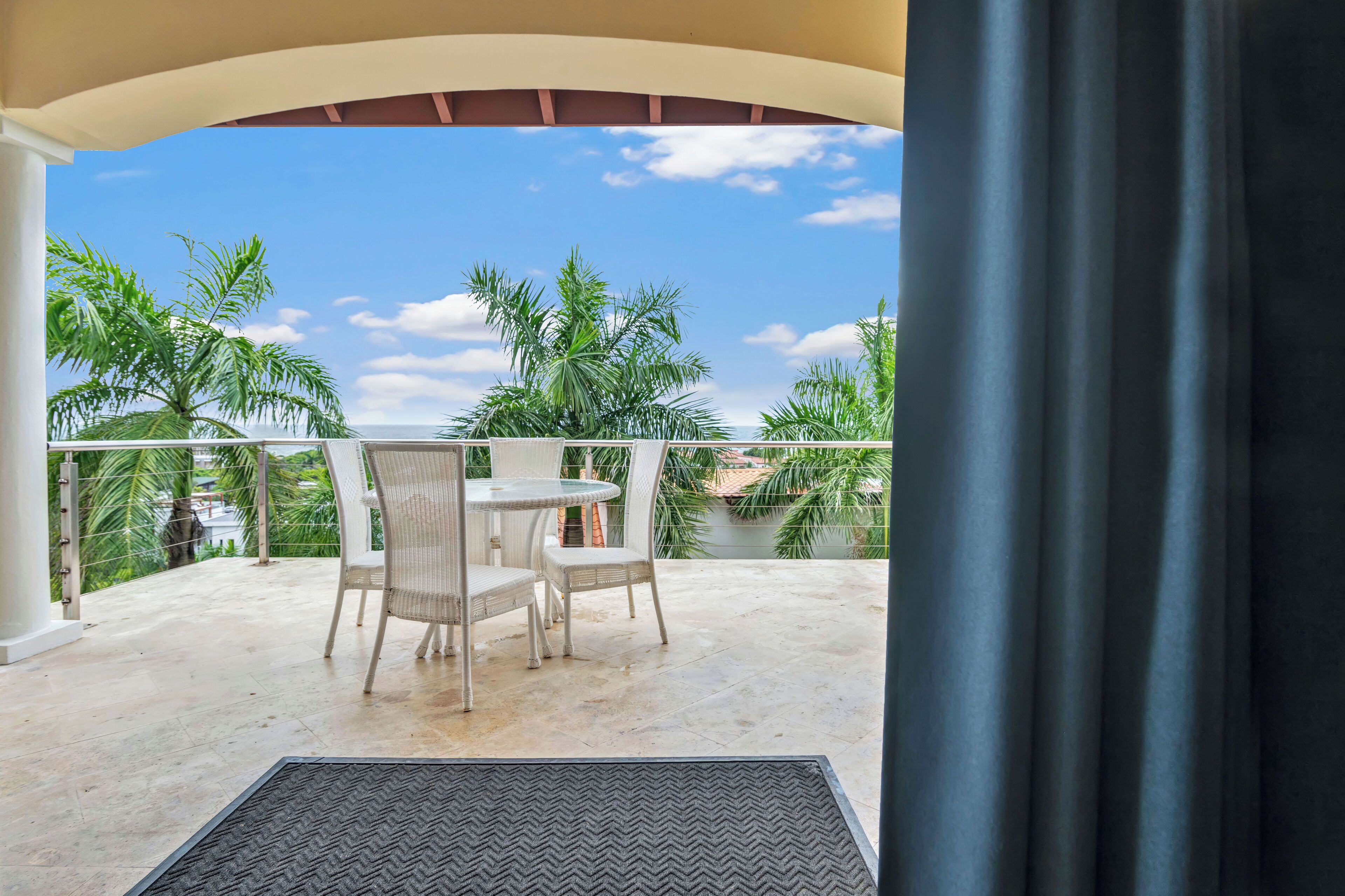 A balcony with a round table and chairs, overlooking a palm tree and a clear sky.