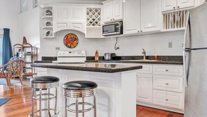 A modern kitchen with white cabinetry, a central island with stools, a microwave, and a stainless steel refrigerator.