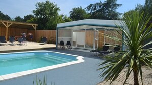 Una piscina con zona cubierta, sillas de descanso y terraza de madera.