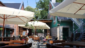 Un espace extérieur aménagé avec des tables et des chaises en bois, protégé par des parasols blancs, et un bâtiment en briques en arrière-plan.