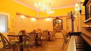 Un coin repas agrémenté d’un piano, de chaises en osier, d’un lustre et d’un mur en pierre.