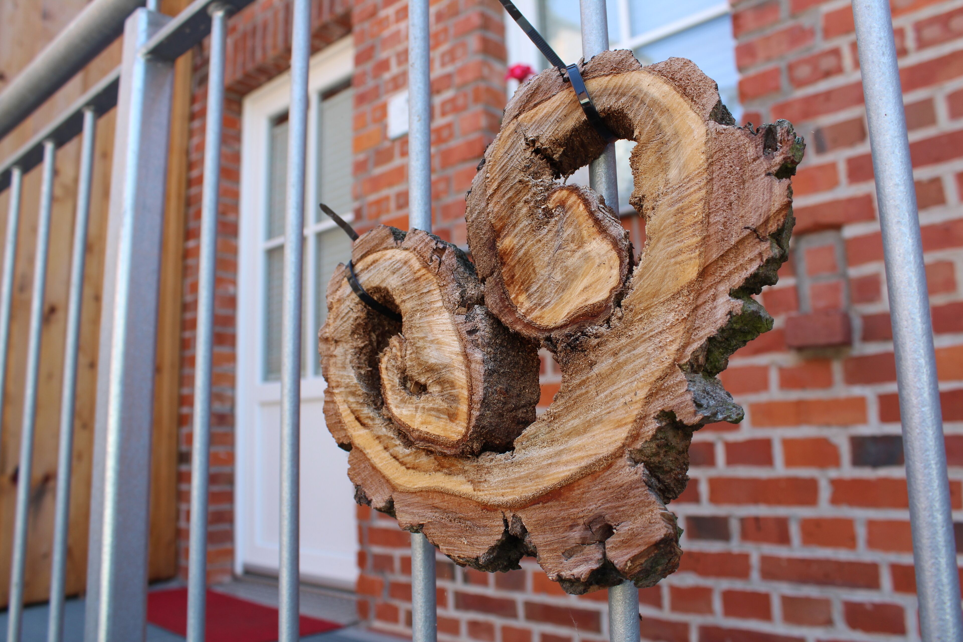 Dos troncos de madera grandes sujetos a un poste metálico, frente a un edificio de ladrillo con una puerta blanca.