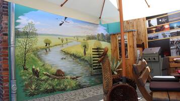 A rustic room with a mural of a river landscape, a wooden chair, and a grill.