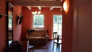 Une pièce avec un plafond en bois, un canapé, une table à manger avec des chaises et de grandes fenêtres laissant entrer la lumière naturelle.