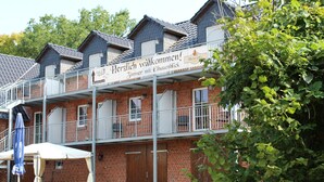Un immeuble de deux étages doté d’un balcon et d’une enseigne sur laquelle on peut lire : « Herzlich willkommen ! Chambres avec vue sur le balcon. »