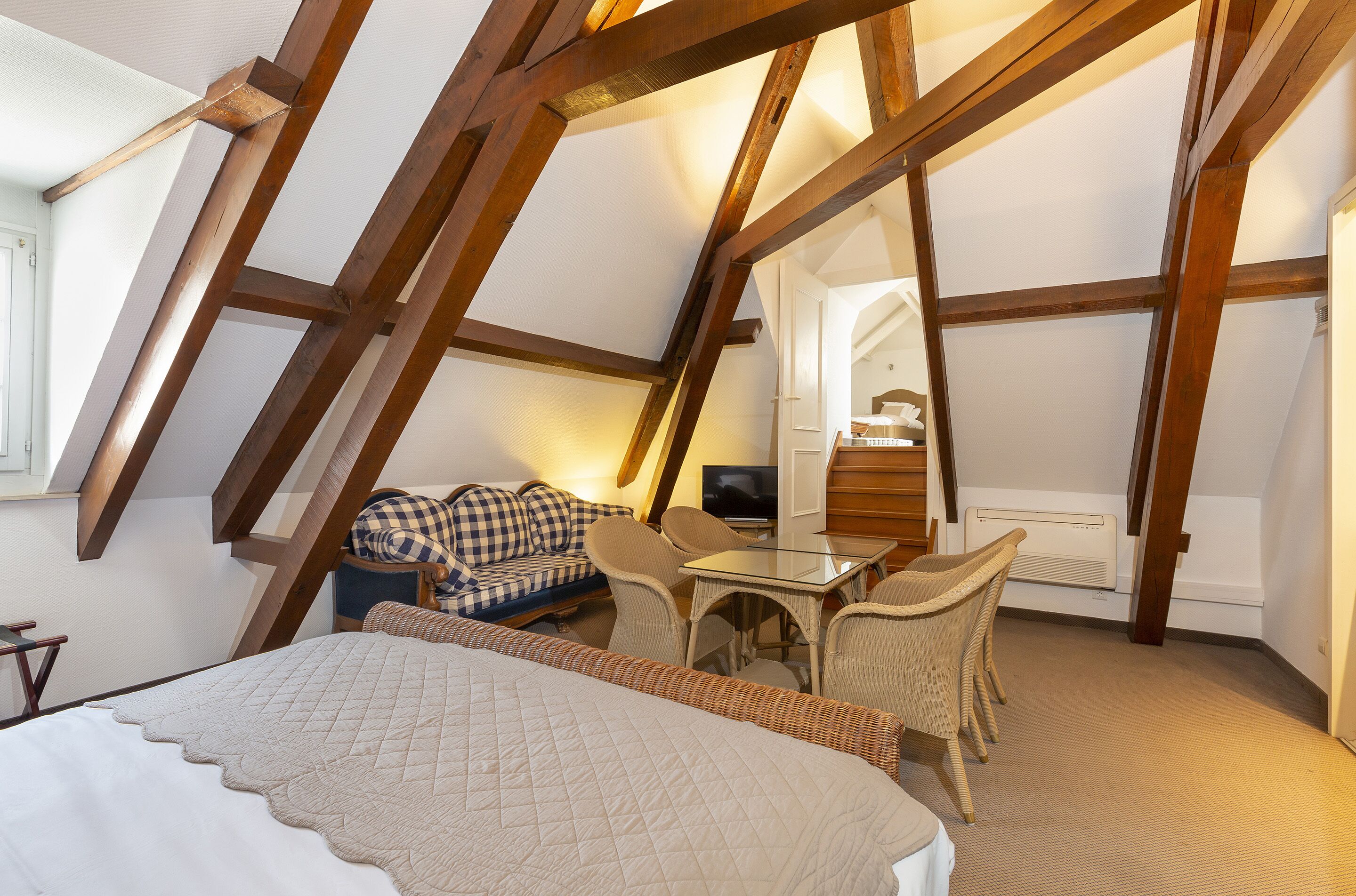 Une chambre confortable située sous les toits, avec des poutres apparentes, un lit, un canapé et une table à manger.