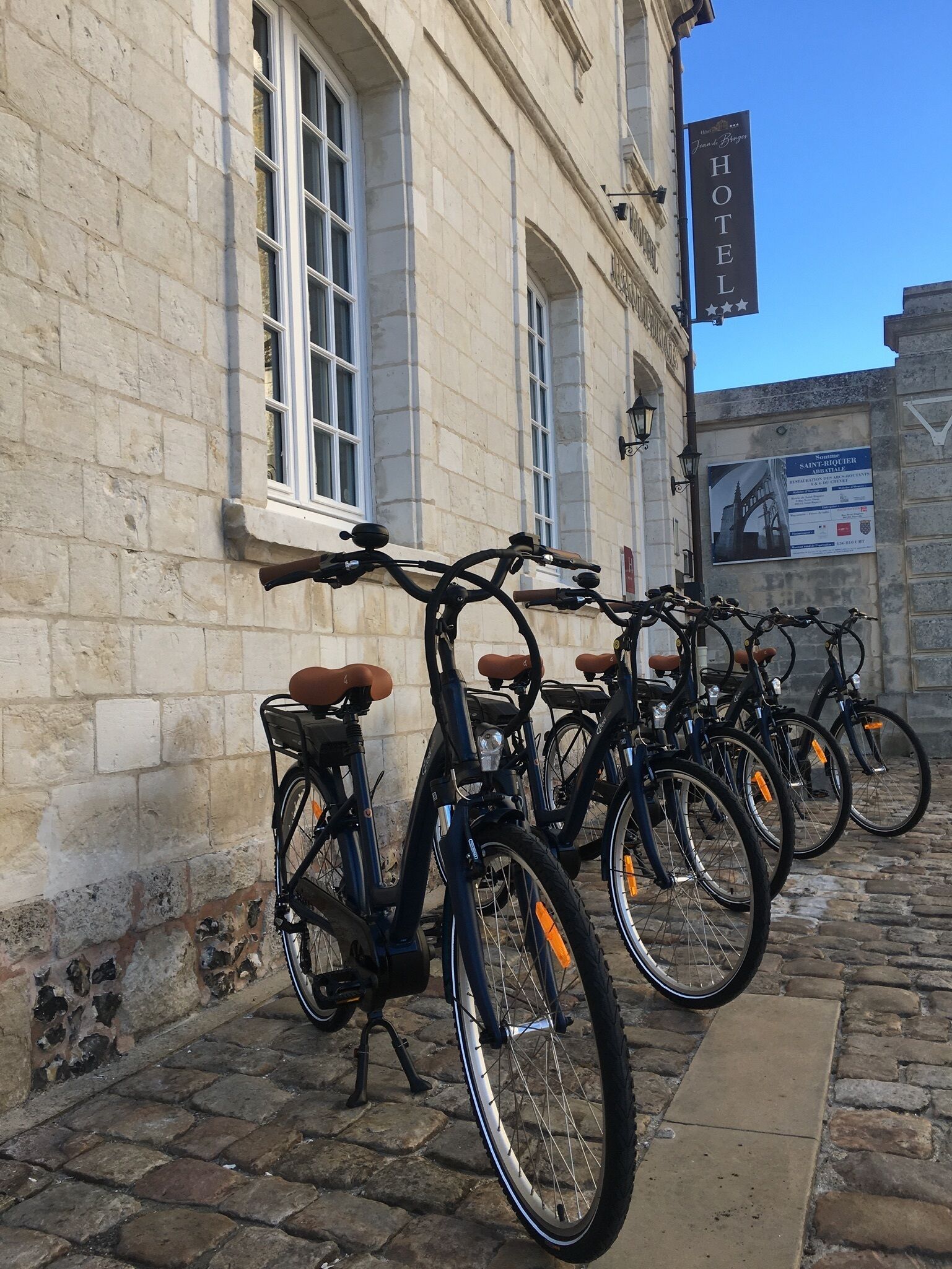 A row of bicycles parked against a stone building with a sign indicating it is a hotel.