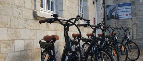 A row of bicycles parked against a stone building with a sign indicating it is a hotel.