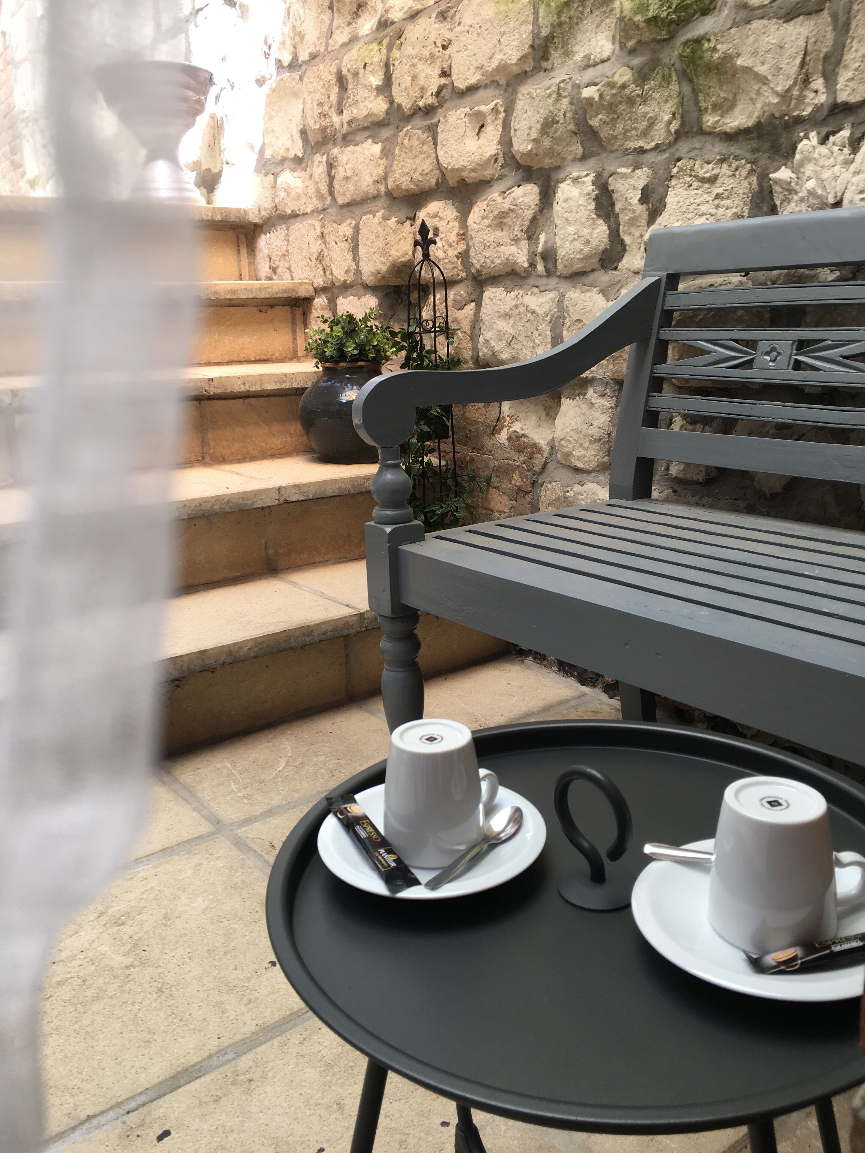 Une table en métal noir avec deux tasses et sous-tasses blanches, une cuillère et une barre de chocolat.